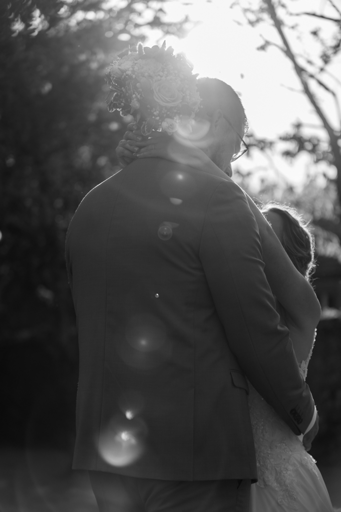 Photographie du mariage d'un couple de jeunes mariés en noir et blanc. La photo est prise à contre jour et le flair de l'objectif rend cette photo très romantique